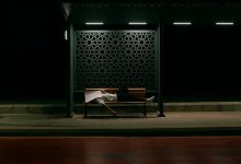 A man sleeping on his back with mouth open, snoring loudly, in a dimly lit bedroom with a blue pillow and white sheets