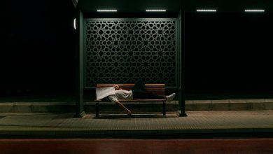 A man sleeping on his back with mouth open, snoring loudly, in a dimly lit bedroom with a blue pillow and white sheets