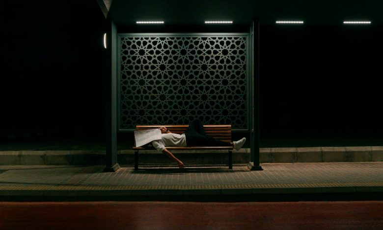 A man sleeping on his back with mouth open, snoring loudly, in a dimly lit bedroom with a blue pillow and white sheets