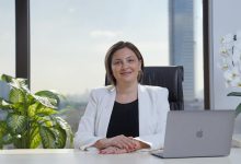 Sabriye Şengül smiling outdoors, wearing a black jacket with her hair tied back, background of blurred greenery