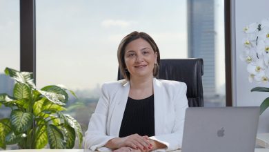 Sabriye Şengül smiling outdoors, wearing a black jacket with her hair tied back, background of blurred greenery