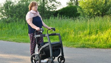 Elderly woman holding a walking aid in a park, highlighting mobility challenges associated with Parkinson's disease